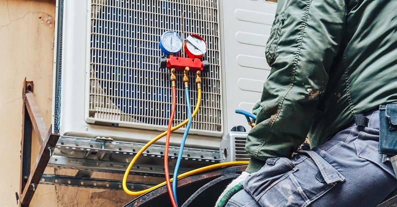 Technician connecting refrigerant gauges to an outdoor AC unit during an AC repair