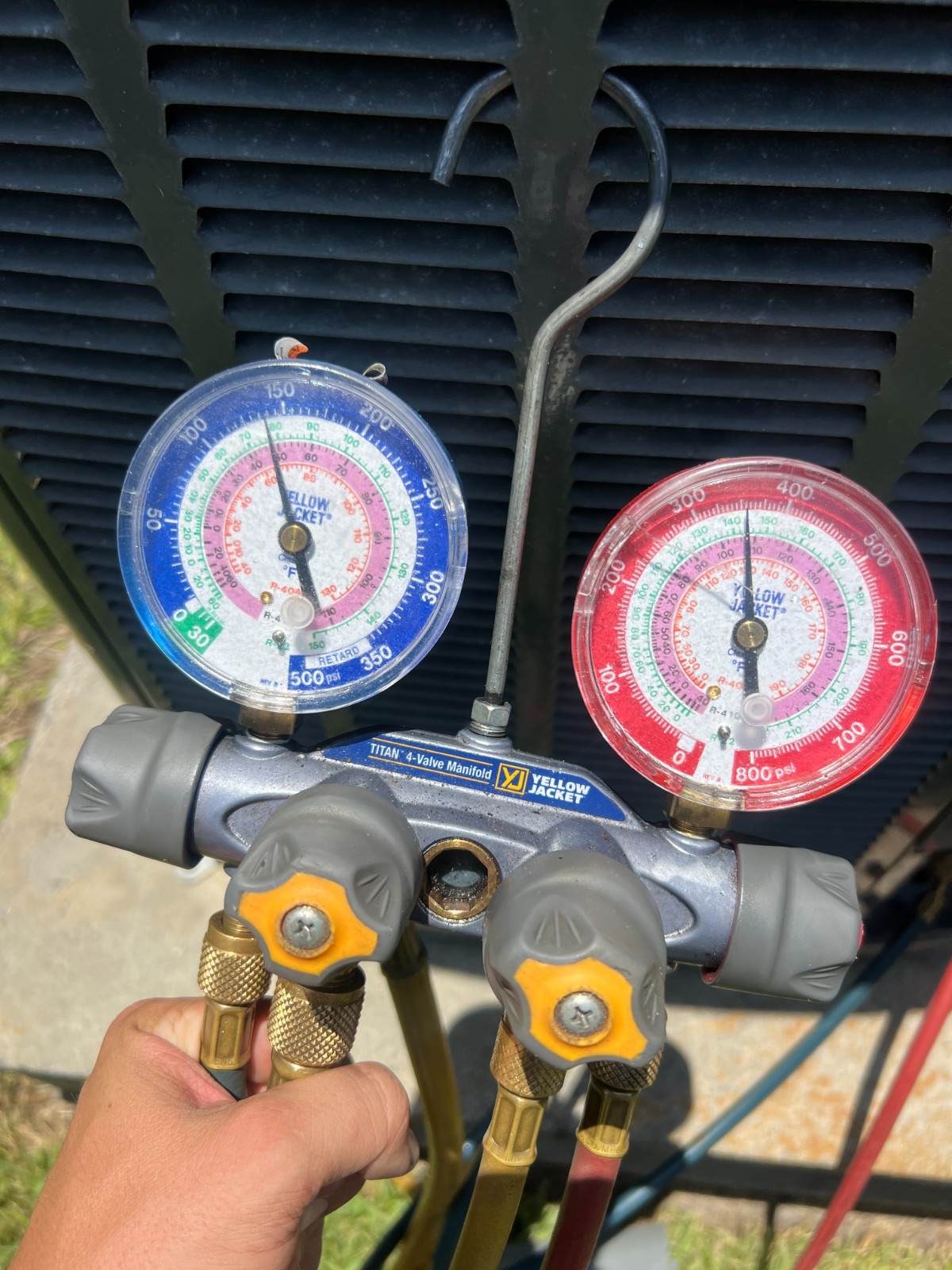 Technician reading manifold gauges connected to an air conditioner during an AC repair