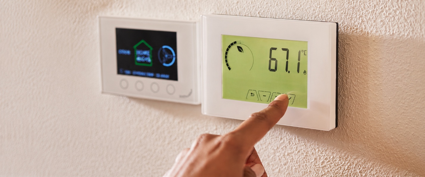 Hand adjusting a programmable thermostat beside a smart thermostat in a Pinellas County, FL home