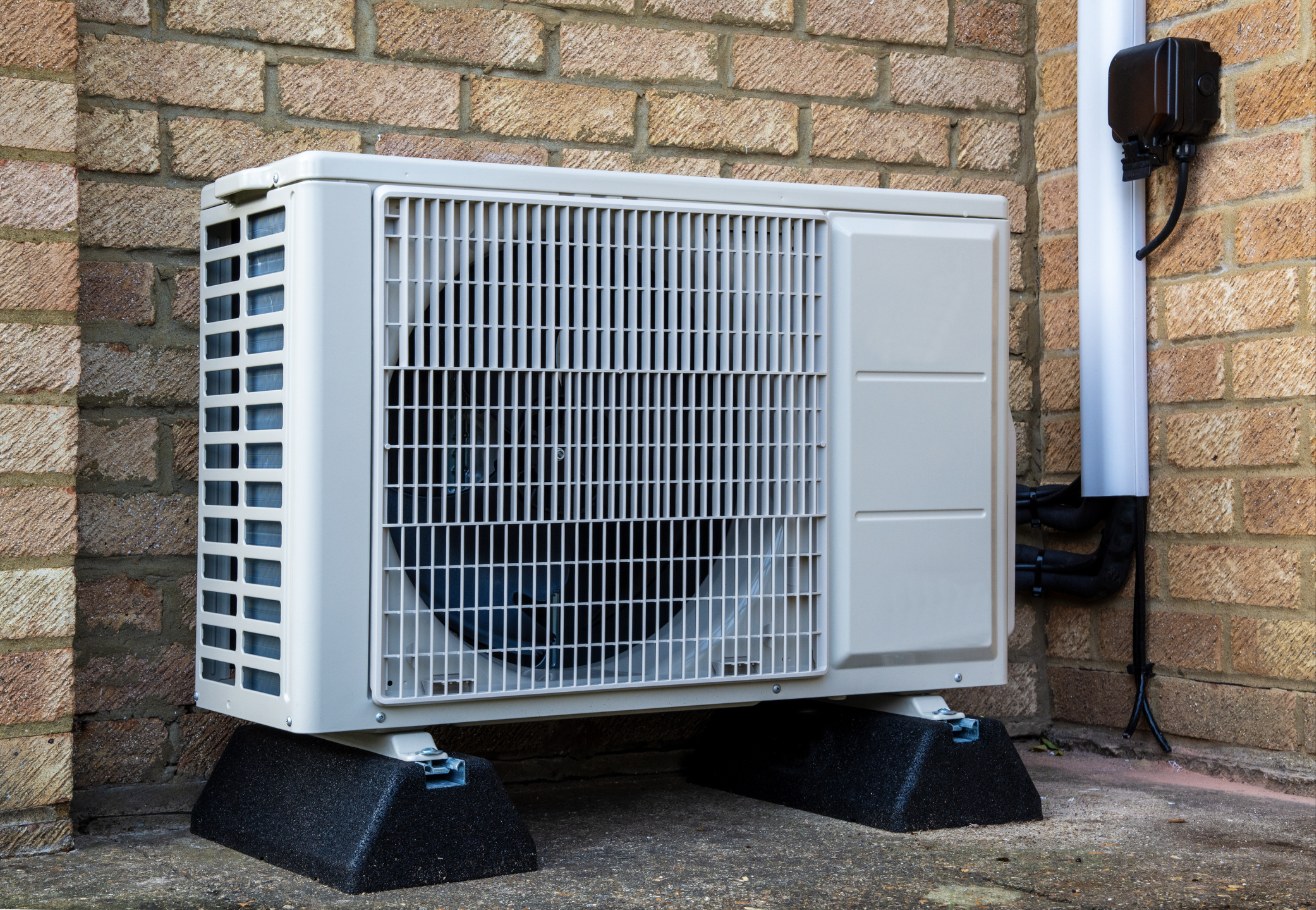 Outdoor heat pump unit mounted beside a brick wall