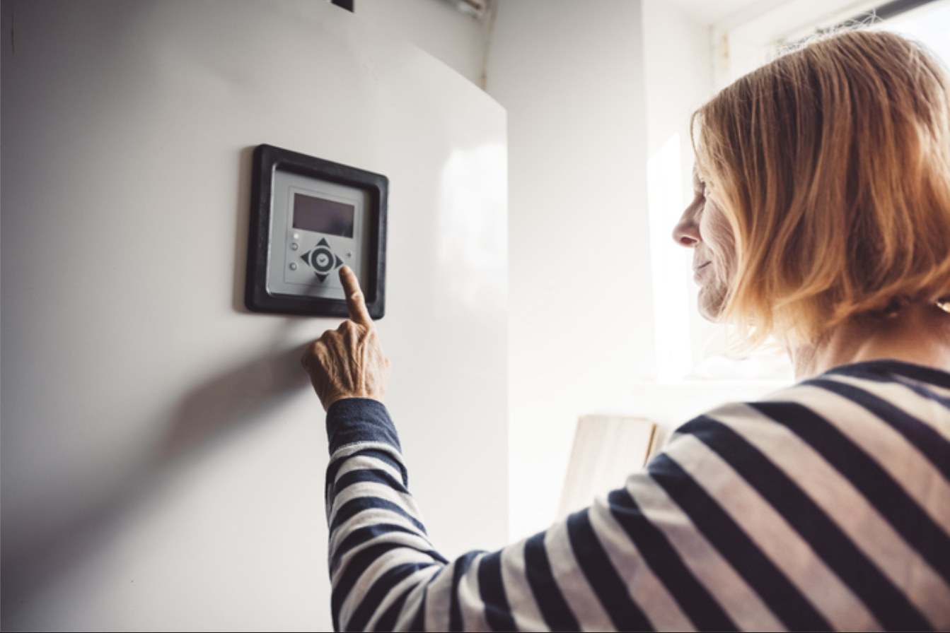 Homeowner adjusting a wall thermostat to save energy